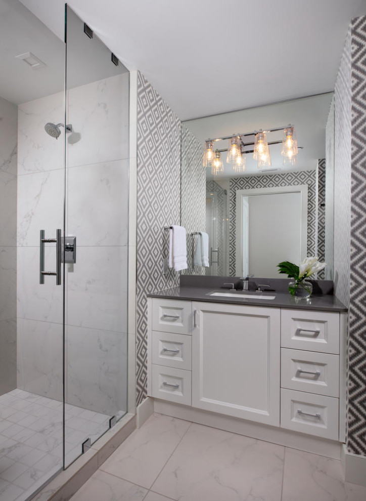 Mid-sized beach style kids bathroom in Miami with shaker cabinets, white cabinets, an alcove shower, a one-piece toilet, white tile, porcelain tile, grey walls, porcelain floors, an undermount sink, engineered quartz benchtops, white floor, a hinged shower door, grey benchtops, a single vanity, a built-in vanity and wallpaper.