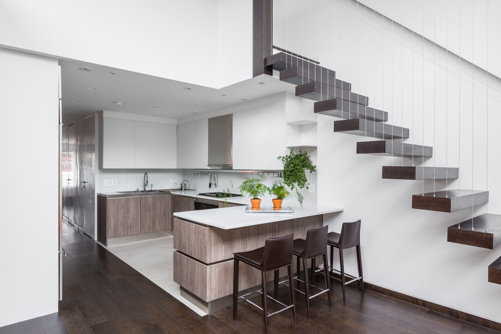 This is an example of a mid-sized contemporary l-shaped open plan kitchen in Milan with flat-panel cabinets, medium wood cabinets, quartz benchtops, white splashback, stainless steel appliances, a peninsula and white floor.