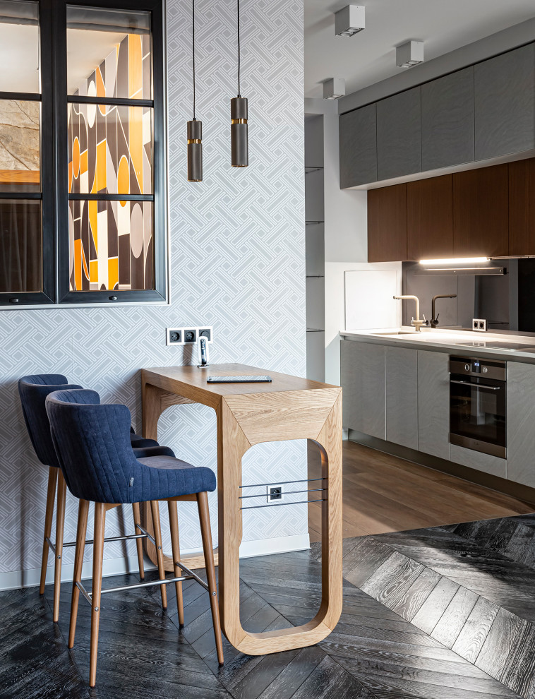Inspiration for a small contemporary galley kitchen in Saint Petersburg with a drop-in sink, flat-panel cabinets, white cabinets, black splashback, glass sheet splashback, black appliances, laminate floors, brown floor and grey benchtop.
