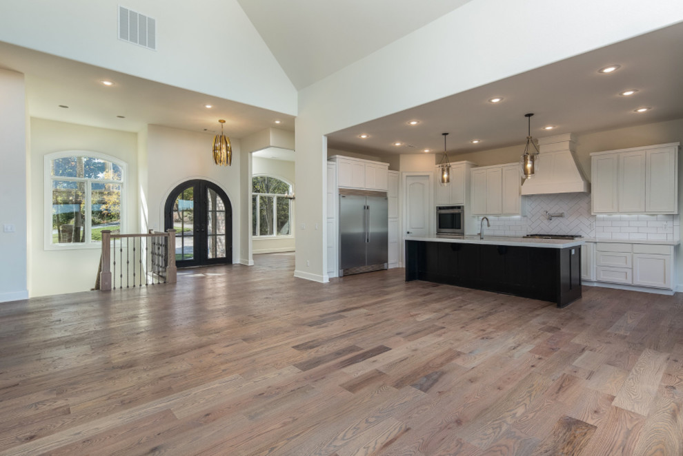 Mid-sized transitional l-shaped dark wood floor and brown floor open concept kitchen photo with an undermount sink, shaker cabinets, white cabinets, solid surface countertops, white backsplash, subway tile backsplash, stainless steel appliances and an island