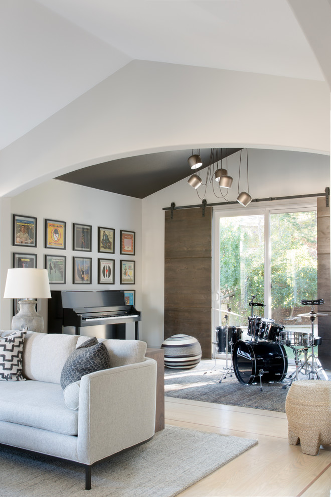 This is an example of a mid-sized transitional open concept family room in San Francisco with light hardwood floors, a standard fireplace, a stone fireplace surround, brown floor, a music area and white walls.