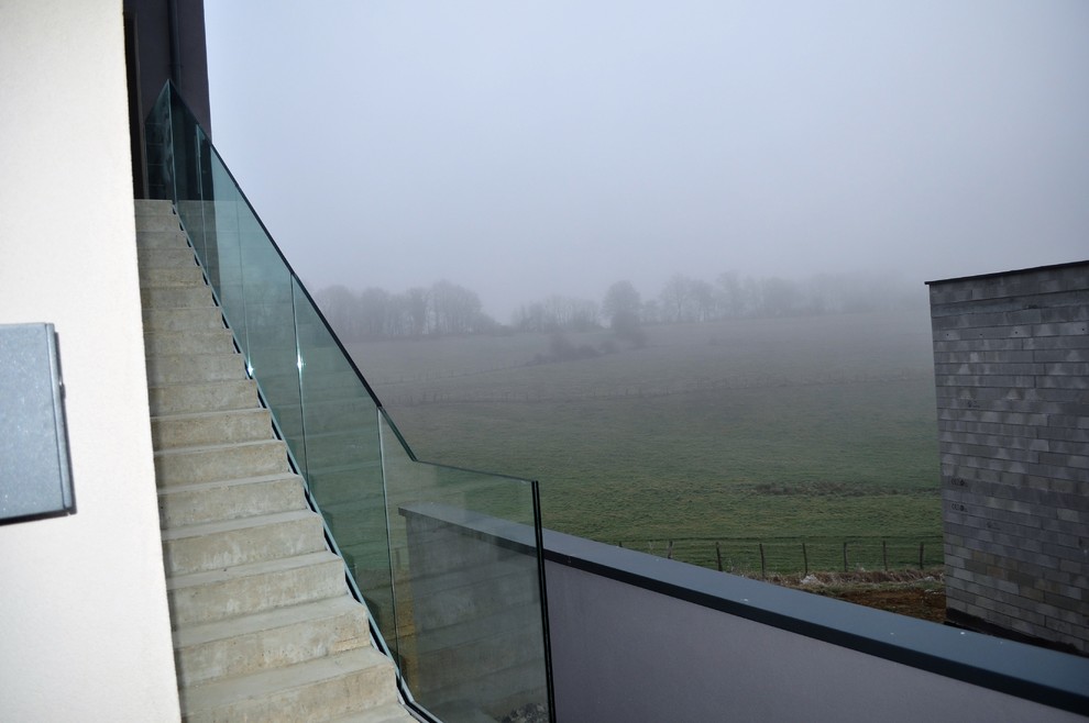 Photo of a large contemporary concrete straight staircase in Dijon with concrete risers and glass railing.