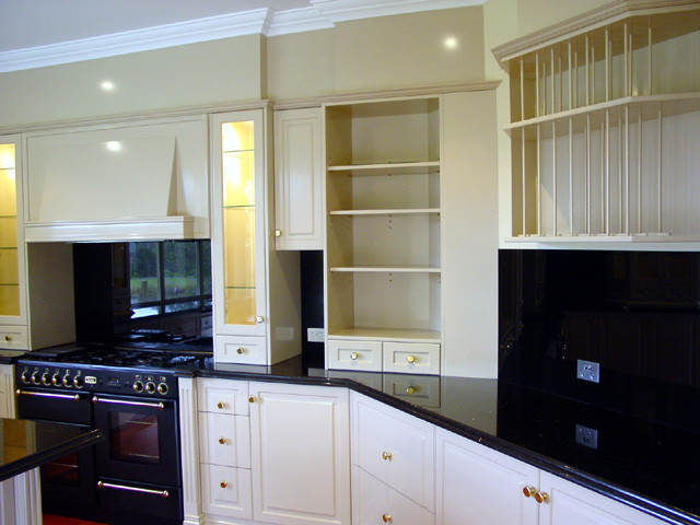 Inspiration for a country u-shaped open plan kitchen in Brisbane with an undermount sink, raised-panel cabinets, white cabinets, granite benchtops, black splashback, stone slab splashback, black appliances, medium hardwood floors and with island.