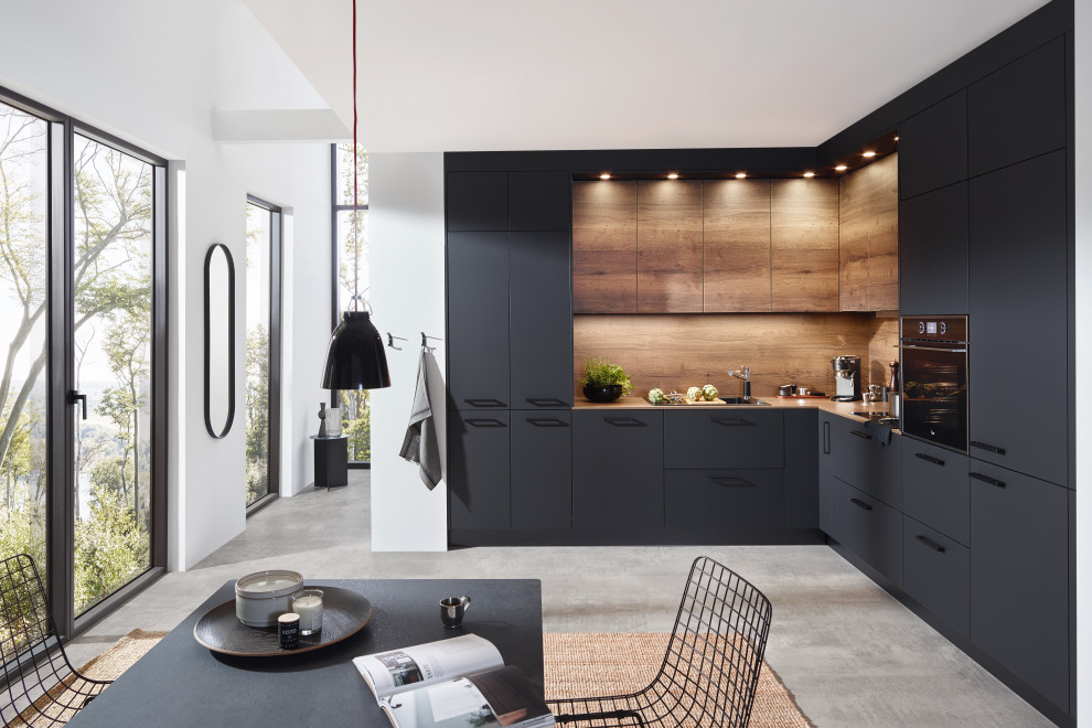This is an example of a mid-sized scandinavian l-shaped separate kitchen in Atlanta with a drop-in sink, flat-panel cabinets, grey cabinets, laminate benchtops, brown splashback, timber splashback, black appliances, concrete floors, no island, grey floor and brown benchtop.