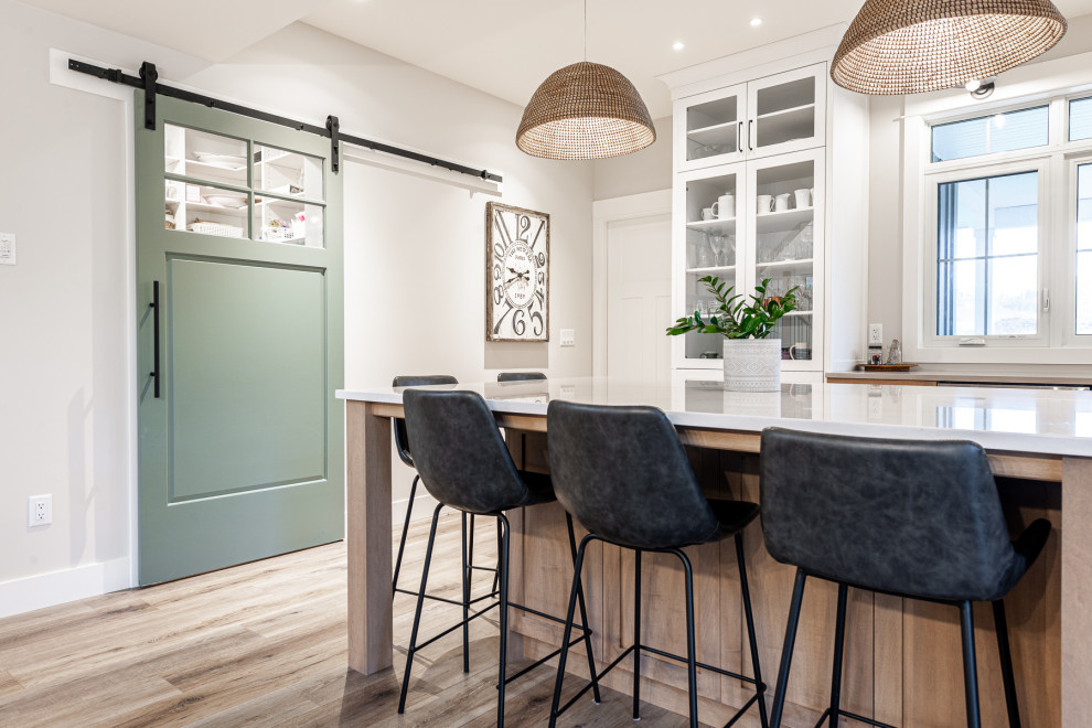 Mid-sized transitional l-shaped laminate floor and brown floor eat-in kitchen photo in Toronto with an undermount sink, recessed-panel cabinets, white cabinets, quartz countertops, stainless steel appliances, an island and white countertops