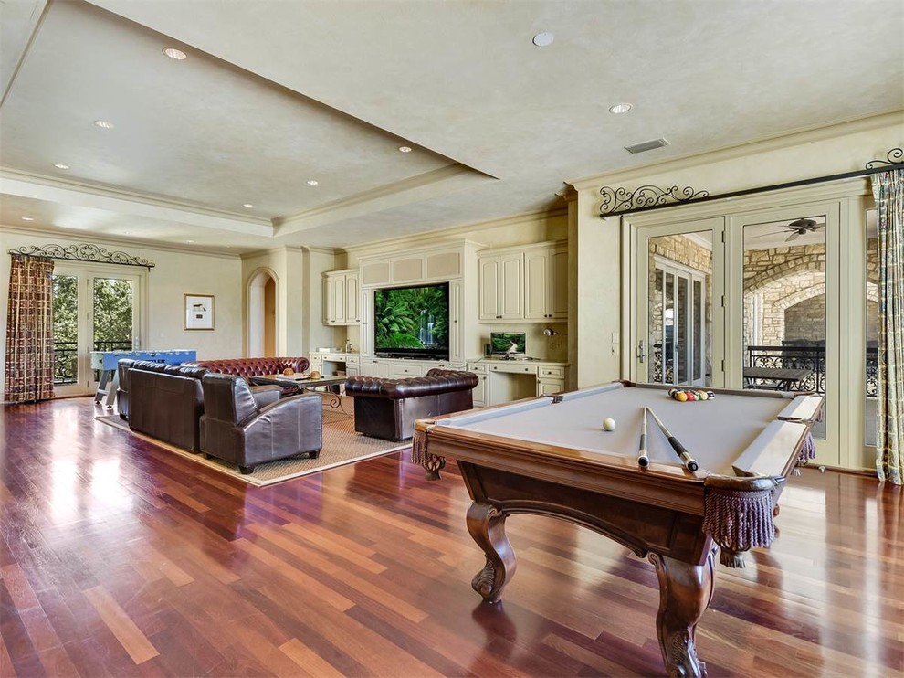Photo of a large traditional open concept family room in Austin with a game room, beige walls, medium hardwood floors, a built-in media wall and brown floor.