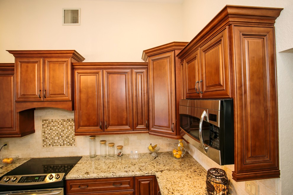 Photo of a mid-sized transitional u-shaped eat-in kitchen in Miami with an undermount sink, raised-panel cabinets, brown cabinets, granite benchtops, beige splashback, stone tile splashback, stainless steel appliances, porcelain floors and a peninsula.