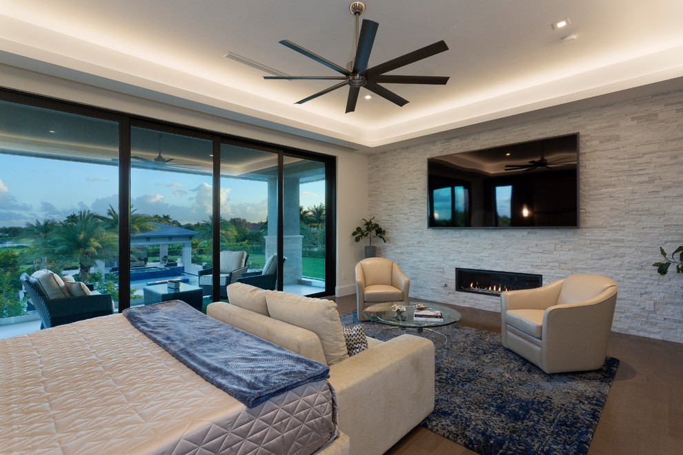 Photo of a large modern master bedroom in Miami with white walls, medium hardwood floors, a ribbon fireplace, a stone fireplace surround and grey floor.