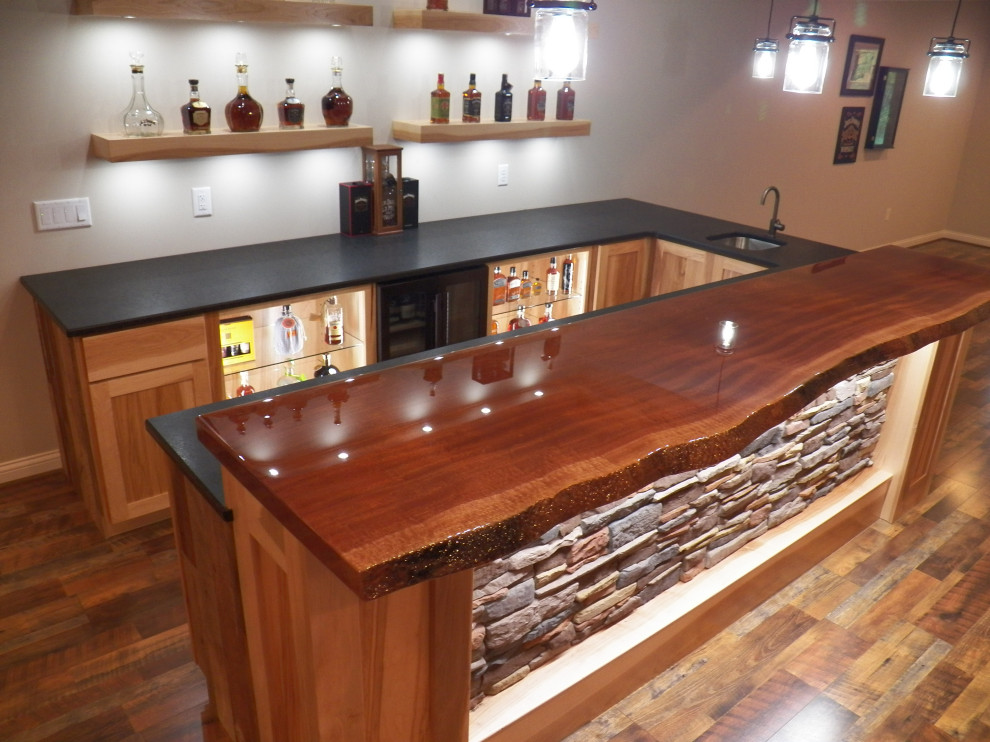 This is an example of a large country u-shaped wet bar in Cincinnati with an undermount sink, shaker cabinets, light wood cabinets, granite benchtops, laminate floors, brown floor and black benchtop.