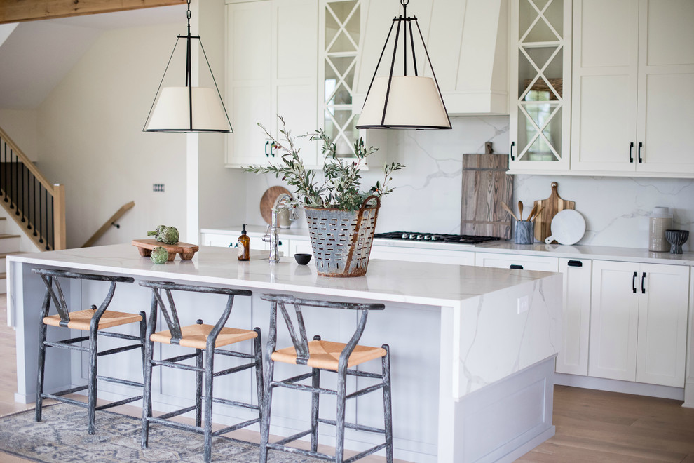 Huge transitional u-shaped light wood floor and brown floor open concept kitchen photo in Indianapolis with a farmhouse sink, shaker cabinets, white cabinets, quartzite countertops, white backsplash, marble backsplash, stainless steel appliances and an island