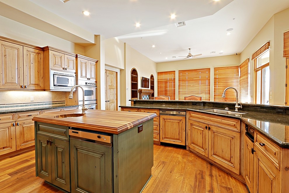 Photo of a large kitchen in Phoenix with raised-panel cabinets, light wood cabinets, granite benchtops, beige splashback, panelled appliances, light hardwood floors and multiple islands.