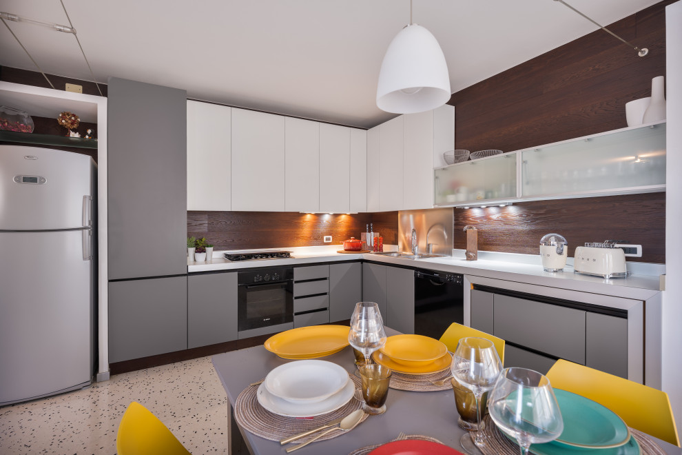 Photo of a mid-sized contemporary l-shaped eat-in kitchen in Venice with a double-bowl sink, flat-panel cabinets, beige cabinets, laminate benchtops, metallic splashback, black appliances, terrazzo floors, no island, white floor and beige benchtop.