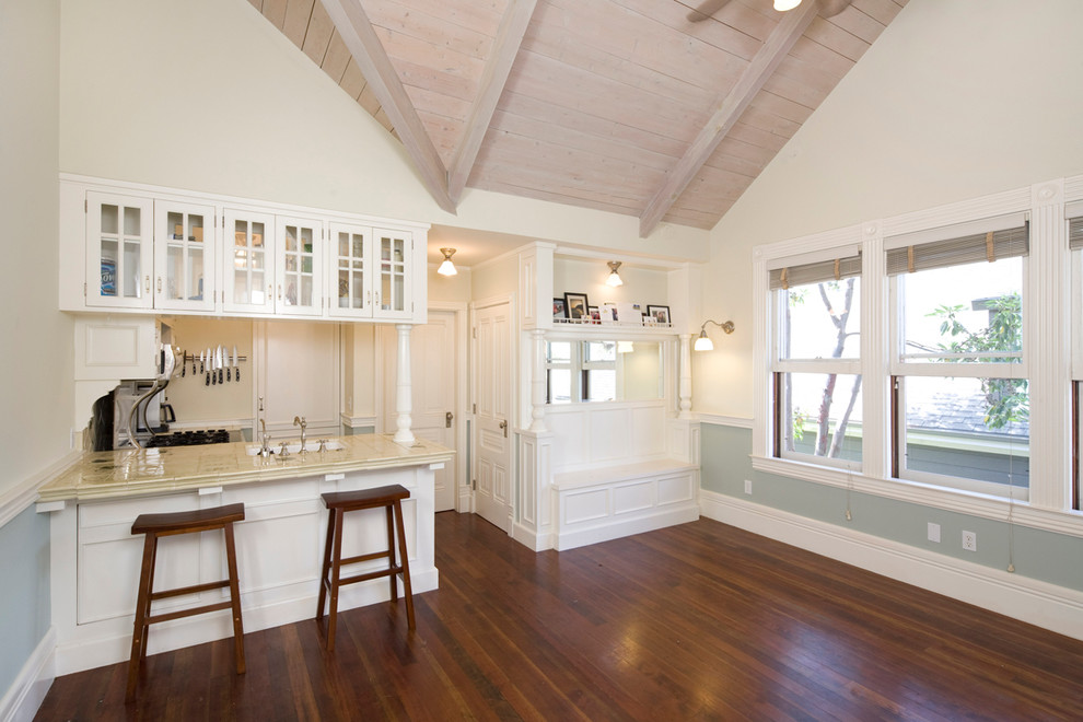 This is an example of a mid-sized traditional l-shaped eat-in kitchen in Santa Barbara with glass-front cabinets, white cabinets, tile benchtops, multi-coloured splashback, stainless steel appliances, an integrated sink, dark hardwood floors and no island.