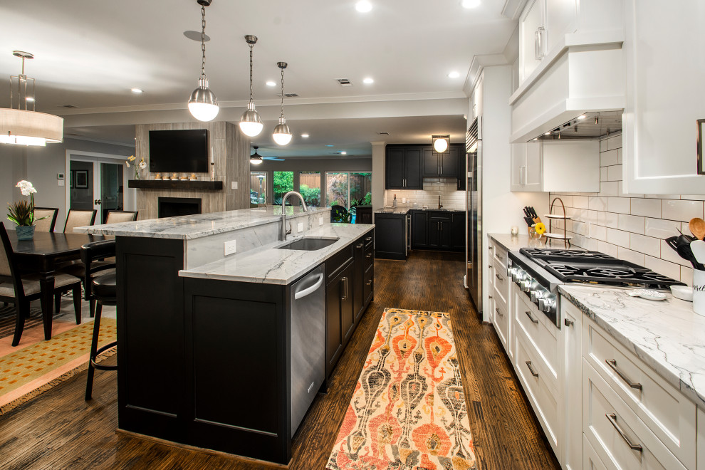 Mid-sized transitional single-wall open plan kitchen in Dallas with dark hardwood floors, brown floor, a double-bowl sink, recessed-panel cabinets, white cabinets, quartz benchtops, white splashback, ceramic splashback, stainless steel appliances, with island and grey benchtop.