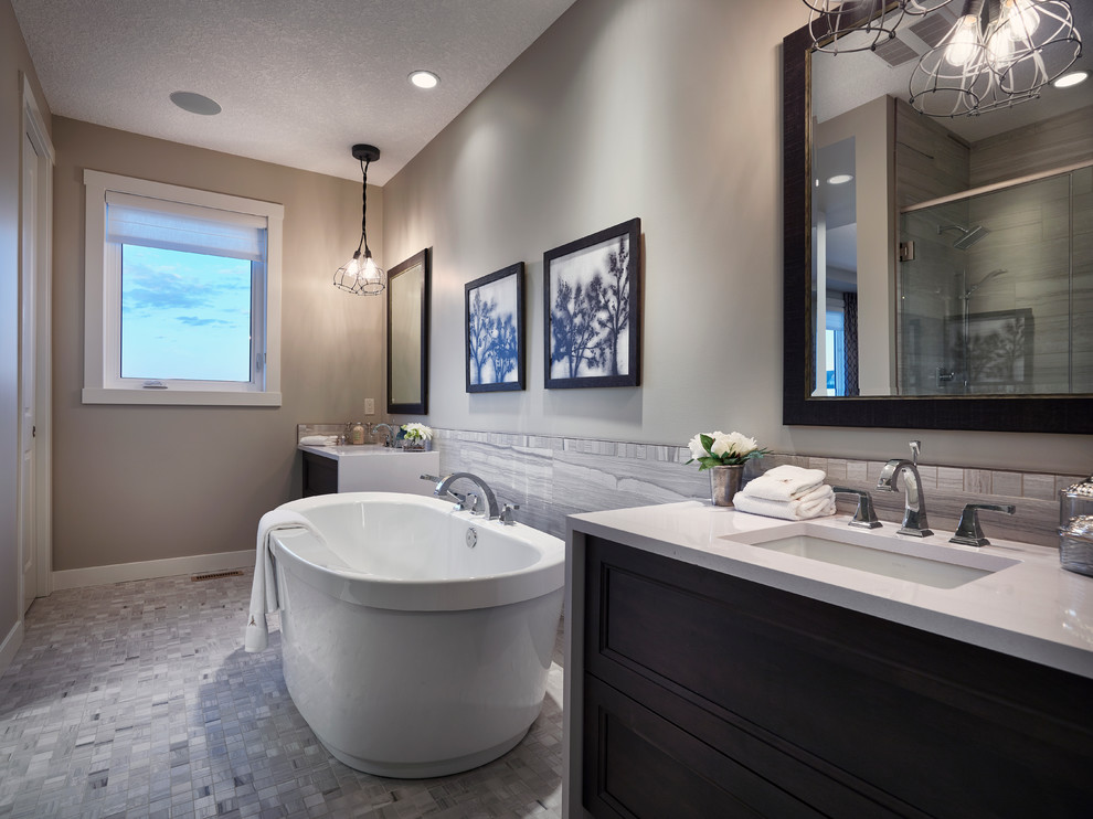 Inspiration for a mid-sized transitional master gray tile and ceramic tile ceramic tile freestanding bathtub remodel in Calgary with an undermount sink, recessed-panel cabinets, dark wood cabinets, marble countertops, a one-piece toilet and gray walls