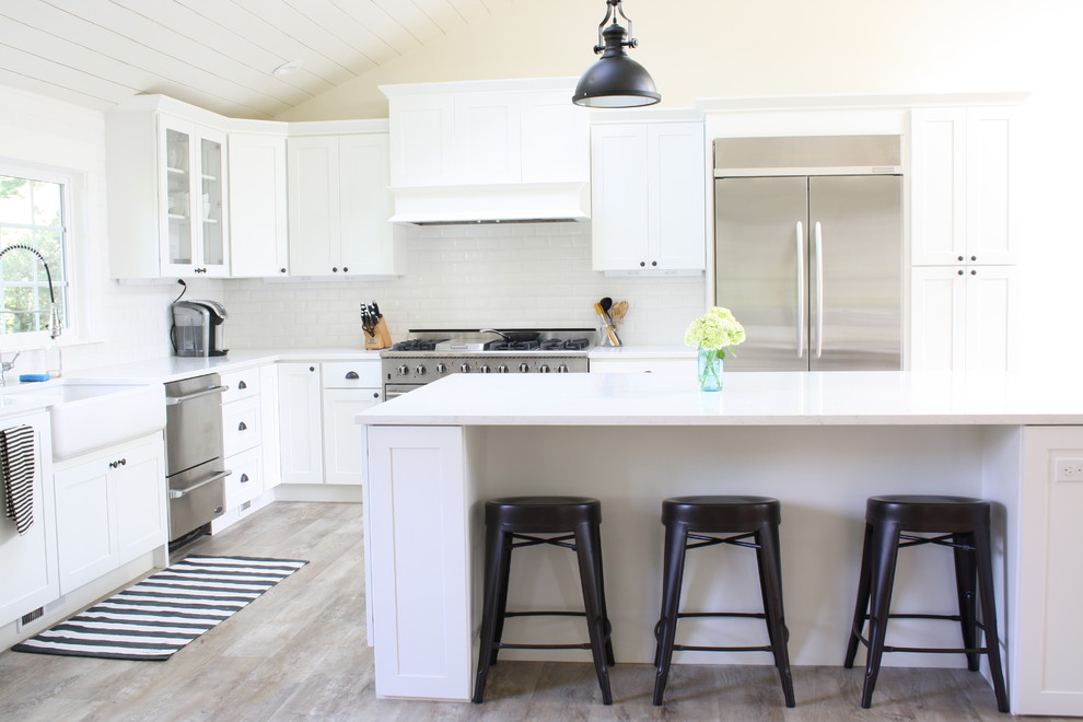 Design ideas for a large country l-shaped open plan kitchen in Seattle with a farmhouse sink, shaker cabinets, white cabinets, quartz benchtops, white splashback, subway tile splashback, stainless steel appliances, vinyl floors and with island.