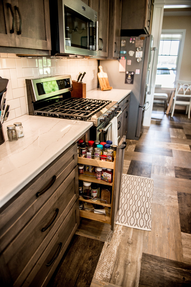 Large transitional l-shaped vinyl floor and multicolored floor open concept kitchen photo with a farmhouse sink, shaker cabinets, gray cabinets, quartz countertops, white backsplash, subway tile backsplash, stainless steel appliances, an island and white countertops