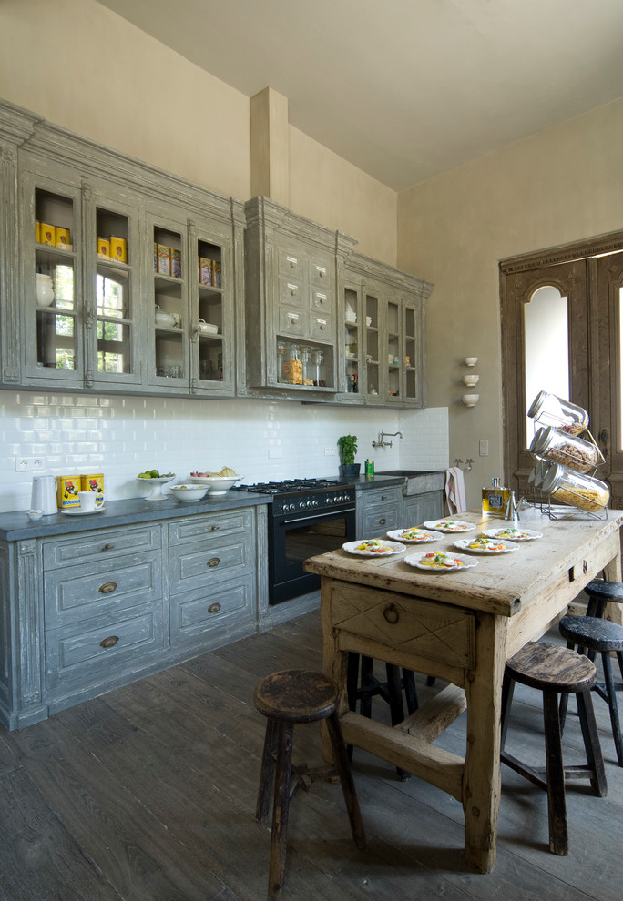 Design ideas for a large mediterranean single-wall eat-in kitchen in Nice with a farmhouse sink, raised-panel cabinets, grey cabinets, white splashback, subway tile splashback, black appliances, dark hardwood floors and with island.