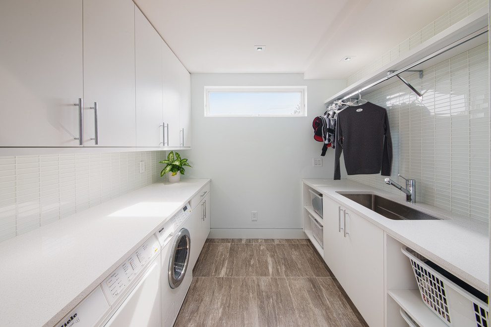 Inspiration for a mid-sized contemporary galley dedicated laundry room in Ottawa with white cabinets, an undermount sink, flat-panel cabinets, quartzite benchtops, white walls, vinyl floors, a side-by-side washer and dryer, brown floor and white benchtop.