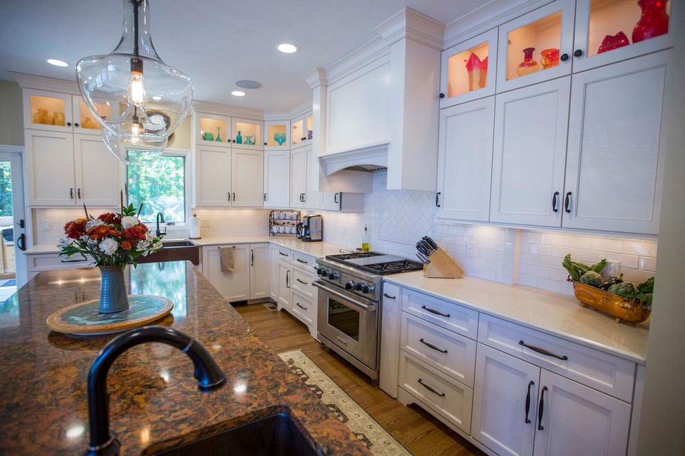 Inspiration for a large transitional l-shaped light wood floor and brown floor enclosed kitchen remodel with a farmhouse sink, shaker cabinets, white cabinets, solid surface countertops, white backsplash, porcelain backsplash, stainless steel appliances and an island