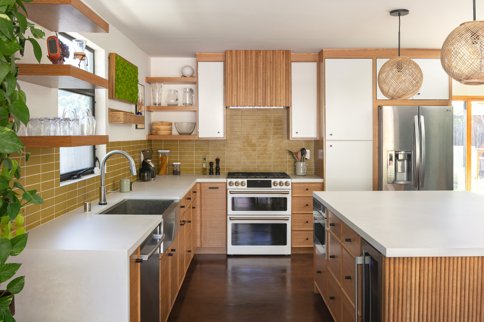 Photo of a large midcentury l-shaped open plan kitchen in Los Angeles with a belfast sink, beaded cabinets, light wood cabinets, engineered stone countertops, green splashback, porcelain splashback, stainless steel appliances, concrete flooring, an island, brown floors and white worktops.