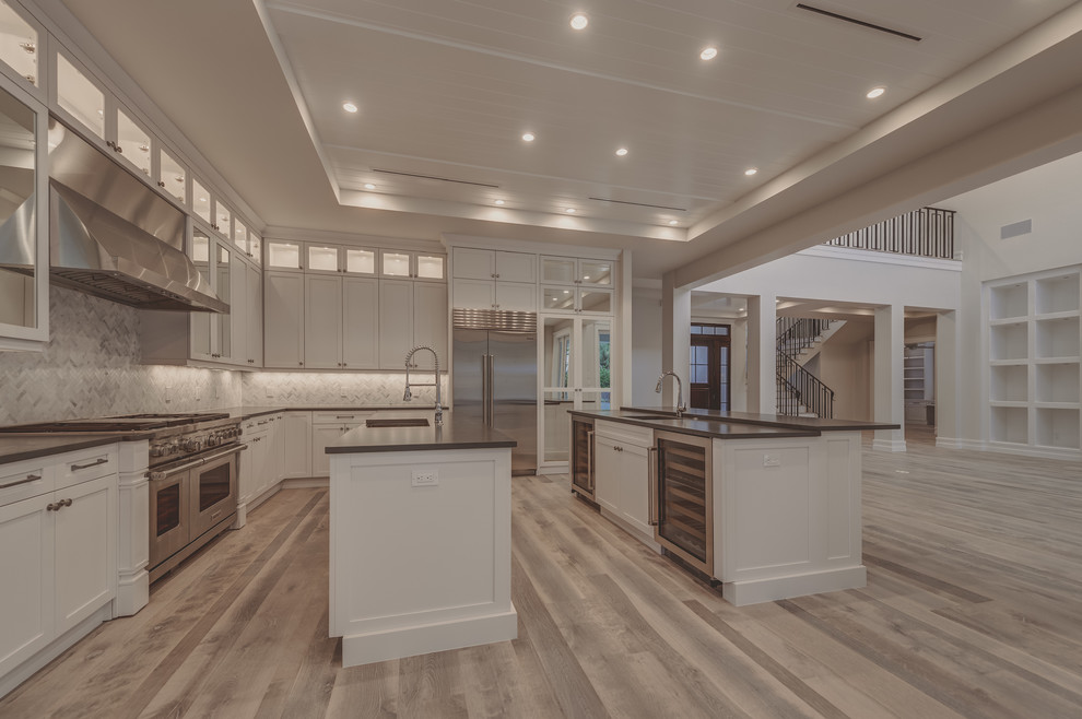 Design ideas for an expansive transitional single-wall open plan kitchen in Miami with a farmhouse sink, recessed-panel cabinets, white cabinets, quartz benchtops, grey splashback, stainless steel appliances, light hardwood floors and multiple islands.