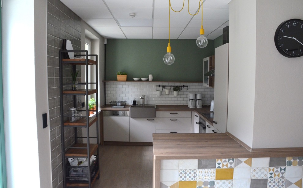 Photo of a small industrial l-shaped open plan kitchen in Berlin with a farmhouse sink, flat-panel cabinets, grey cabinets, wood benchtops, white splashback, subway tile splashback, panelled appliances, linoleum floors and beige floor.