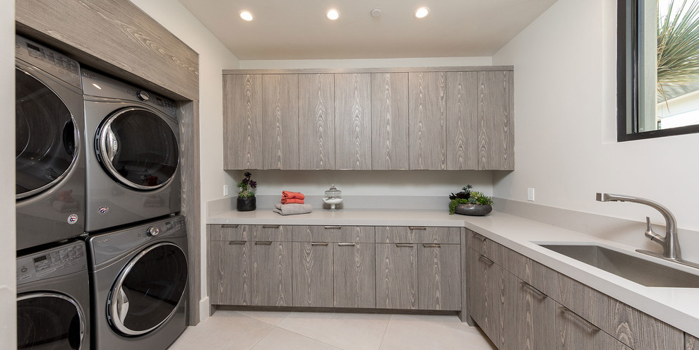 Photo of a contemporary u-shaped laundry room in Other with flat-panel cabinets, grey cabinets, white walls, a side-by-side washer and dryer, beige floor, grey benchtop and an undermount sink.