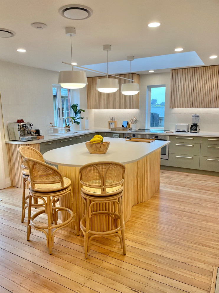 Photo of a Large contemporary L-shaped kitchen pantry in Dunedin With a Double-bowl Sink, Flat-panel Cabinets, Green Cabinets, Quartz Benchtops, White Splashback, Porcelain Splashback, Stainless Steel Appliances, Medium Hardwood Floors, with Island, Brown Floor and White Benchtop.