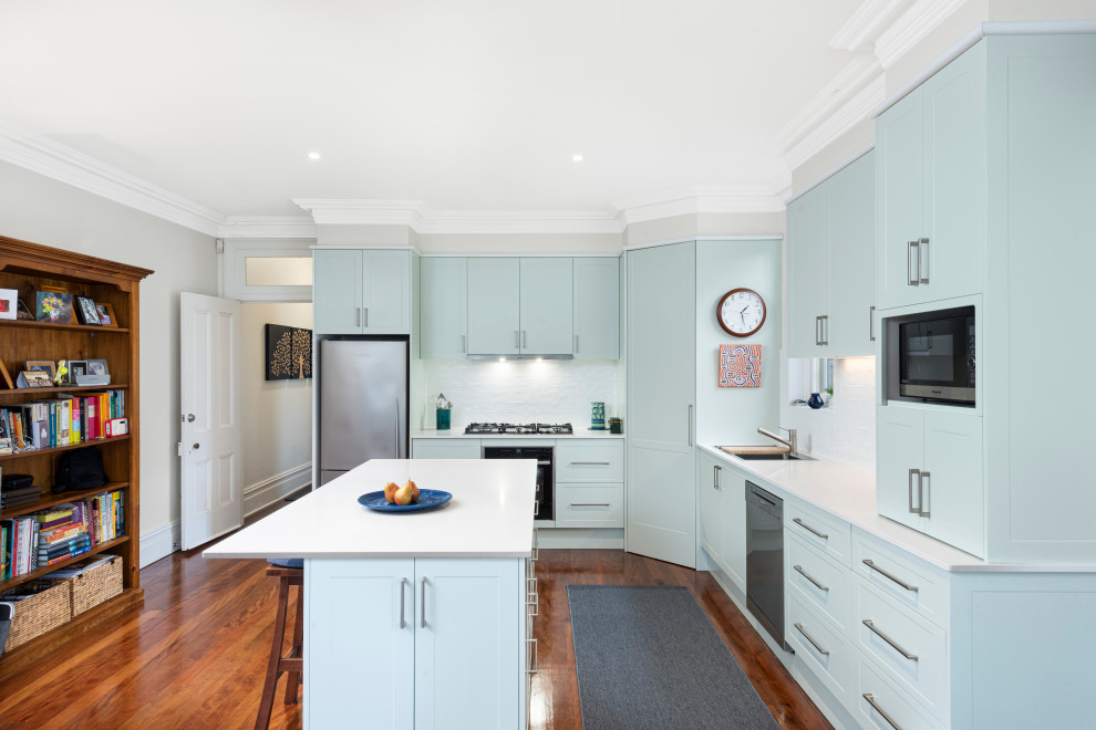 This is an example of a mid-sized modern l-shaped kitchen pantry in Sydney with blue cabinets, quartz benchtops, white splashback, ceramic splashback, stainless steel appliances, with island and white benchtop.