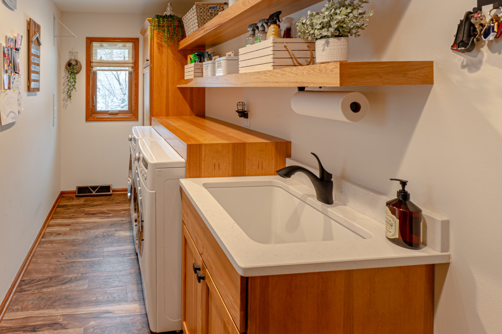 Photo of a small beach style single-wall dedicated laundry room in Milwaukee with an undermount sink, shaker cabinets, medium wood cabinets, wood benchtops, beige walls, medium hardwood floors, a side-by-side washer and dryer, brown floor and brown benchtop.