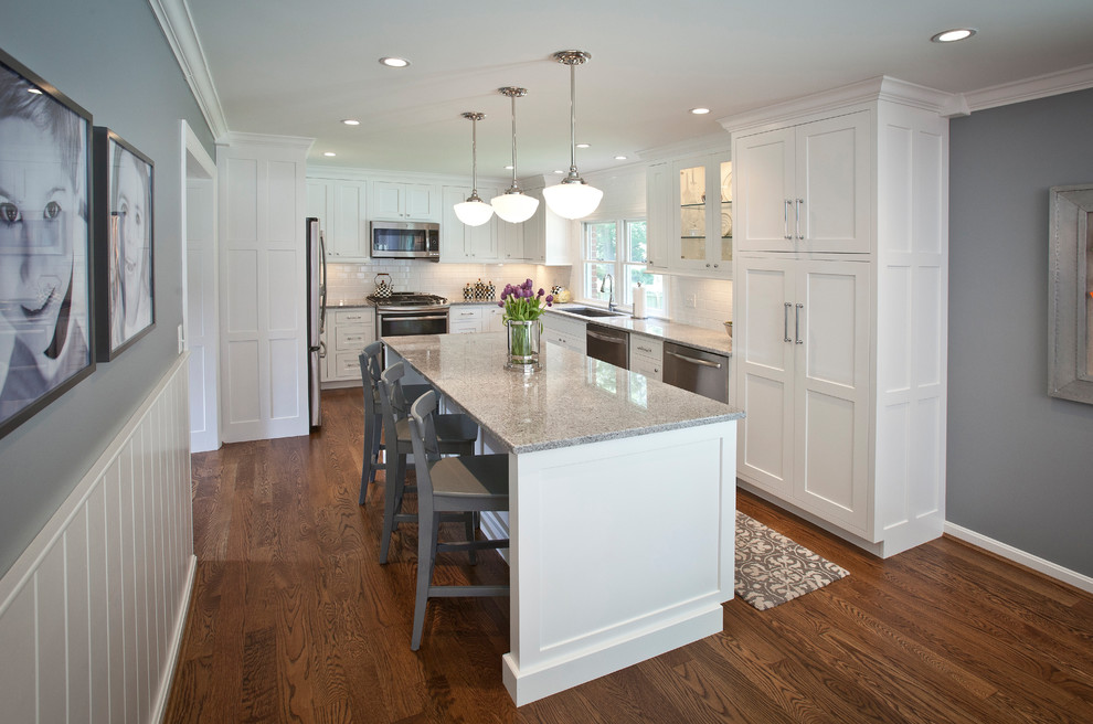 Large country u-shaped eat-in kitchen in Cincinnati with a double-bowl sink, white cabinets, granite benchtops, white splashback, stainless steel appliances, medium hardwood floors, with island, beaded inset cabinets, porcelain splashback and brown floor.