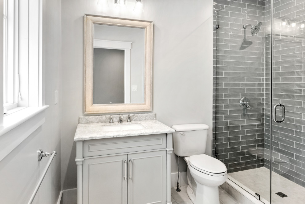 This is an example of a mid-sized country 3/4 bathroom in Boston with furniture-like cabinets, white cabinets, an alcove shower, a one-piece toilet, gray tile, glass tile, grey walls, ceramic floors, an undermount sink, marble benchtops, white floor, a hinged shower door, white benchtops, a single vanity and a freestanding vanity.
