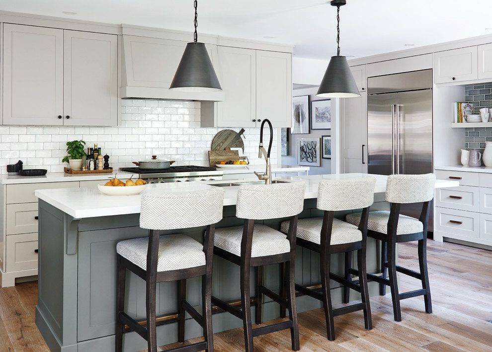 Transitional u-shaped medium tone wood floor and brown floor kitchen photo in Toronto with an undermount sink, shaker cabinets, beige cabinets, white backsplash, glass tile backsplash, stainless steel appliances, an island and white countertops