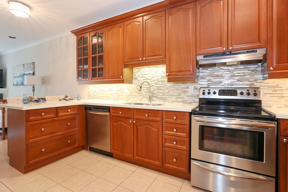 Enclosed kitchen - mid-sized transitional u-shaped porcelain tile and beige floor enclosed kitchen idea in Toronto with an undermount sink, recessed-panel cabinets, brown cabinets, quartz countertops, beige backsplash, mosaic tile backsplash, stainless steel appliances and a peninsula
