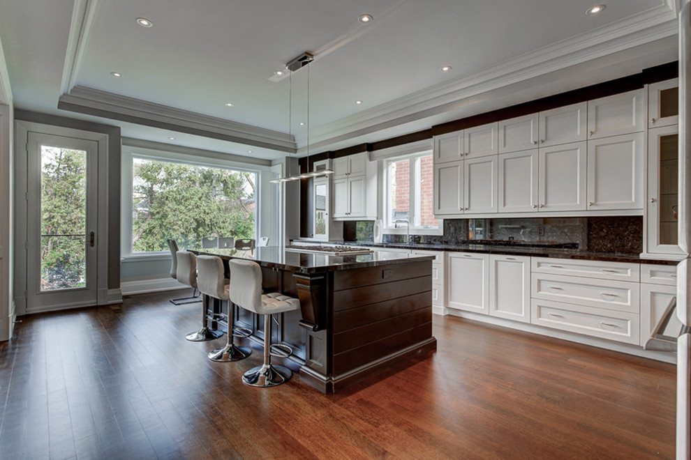 Mid-sized transitional l-shaped medium tone wood floor and brown floor kitchen photo in Toronto with an undermount sink, recessed-panel cabinets, white cabinets, gray backsplash, stainless steel appliances and an island