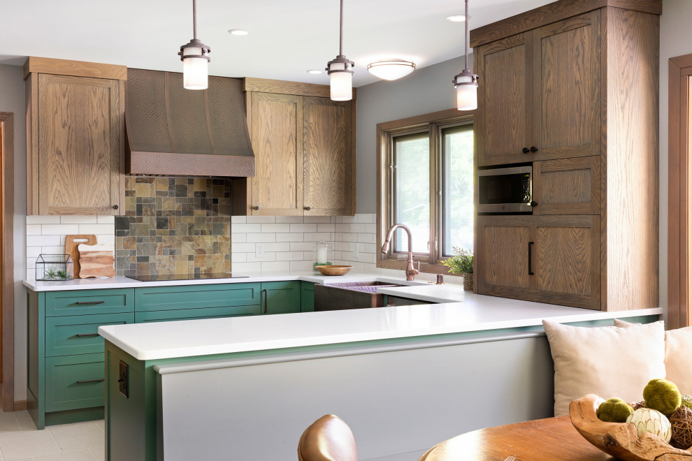 This is an example of a mid-sized transitional u-shaped eat-in kitchen in Minneapolis with a farmhouse sink, shaker cabinets, green cabinets, quartz benchtops, white splashback, porcelain splashback, stainless steel appliances, ceramic floors, a peninsula, grey floor and white benchtop.