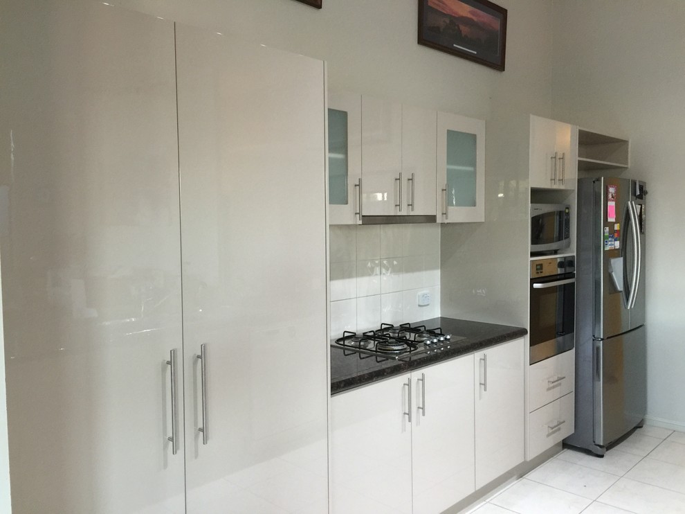 Photo of a mid-sized modern galley open plan kitchen in Brisbane with a drop-in sink, glass-front cabinets, beige cabinets, granite benchtops, beige splashback, ceramic splashback, stainless steel appliances, ceramic floors and with island.