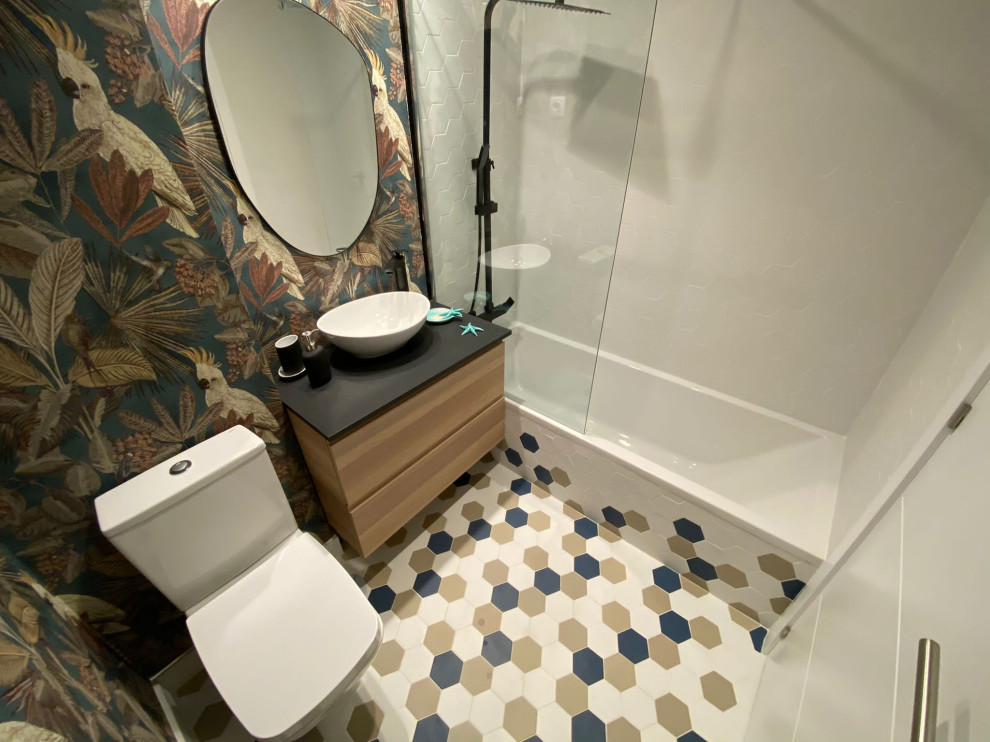 Photo of a mid-sized contemporary powder room in Madrid with furniture-like cabinets, white cabinets, a two-piece toilet, multi-coloured tile, mosaic tile, multi-coloured walls, mosaic tile floors, a vessel sink, marble benchtops, multi-coloured floor, black benchtops, a floating vanity and wallpaper.