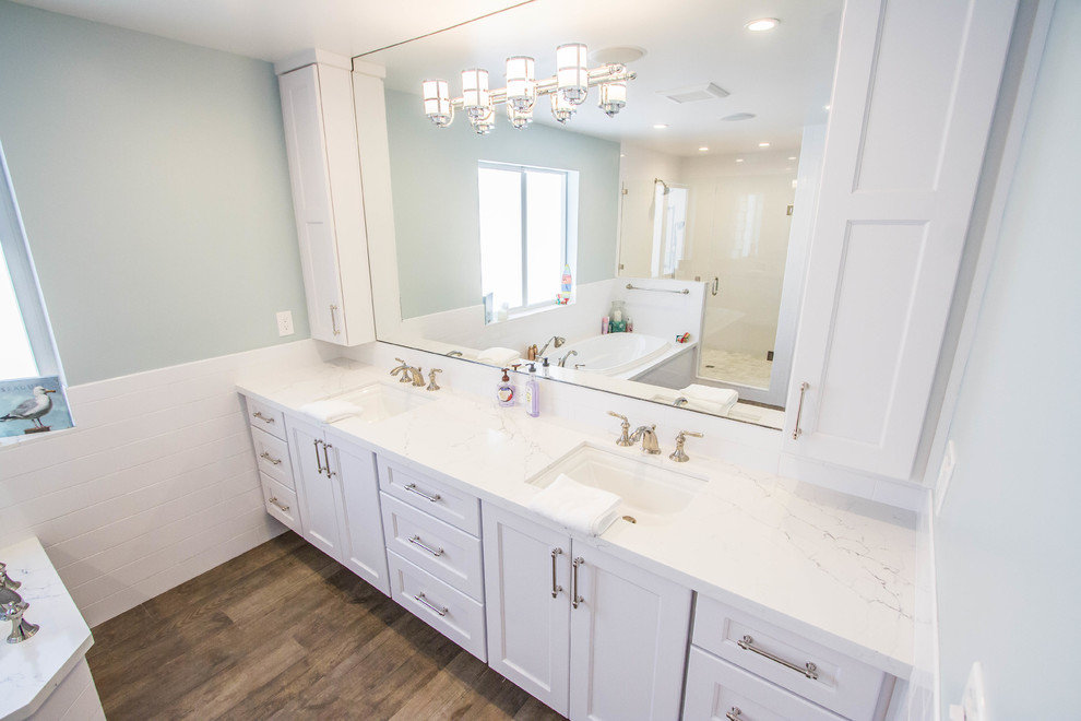 This is an example of a large beach style master bathroom in Miami with shaker cabinets, white cabinets, a drop-in tub, an alcove shower, grey walls, dark hardwood floors, an undermount sink, quartzite benchtops, brown floor, a hinged shower door and white benchtops.