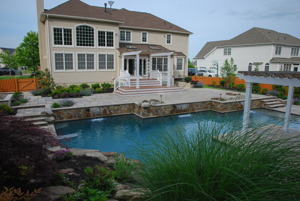 This is an example of a mid-sized traditional backyard custom-shaped natural pool in DC Metro with concrete pavers and a water feature.