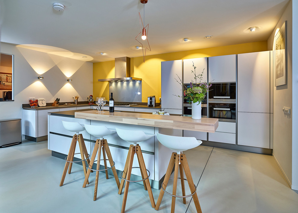 Design ideas for a large contemporary l-shaped open plan kitchen in Other with a drop-in sink, flat-panel cabinets, white cabinets, black appliances, concrete floors and with island.