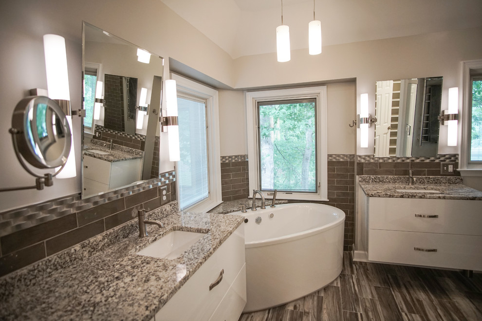 Inspiration for a mid-sized contemporary master bathroom in Atlanta with flat-panel cabinets, white cabinets, a freestanding tub, an alcove shower, a one-piece toilet, brown tile, glass tile, grey walls, ceramic floors, an undermount sink, quartzite benchtops, grey floor, a sliding shower screen and grey benchtops.