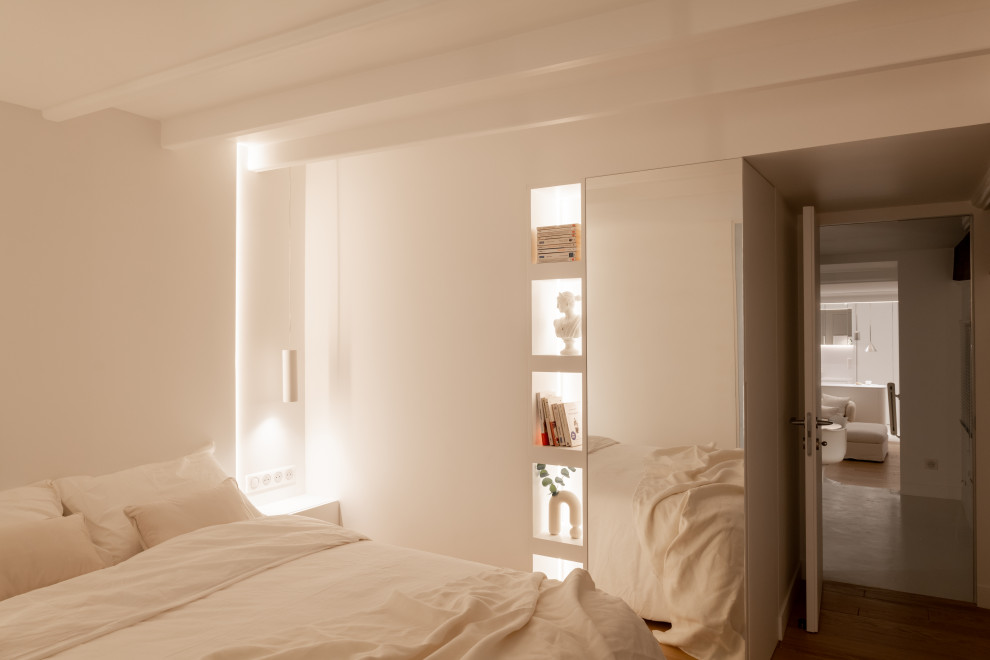 Diseño de dormitorio beige y blanco actual de tamaño medio sin chimenea con paredes blancas, suelo de madera clara y suelo marrón