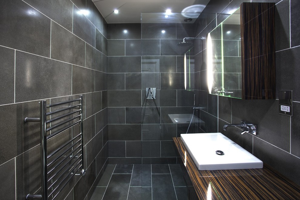 Photo of a mid-sized contemporary bathroom in West Midlands with a console sink, flat-panel cabinets, dark wood cabinets, wood benchtops, a curbless shower, black tile, stone tile, black walls and slate floors.