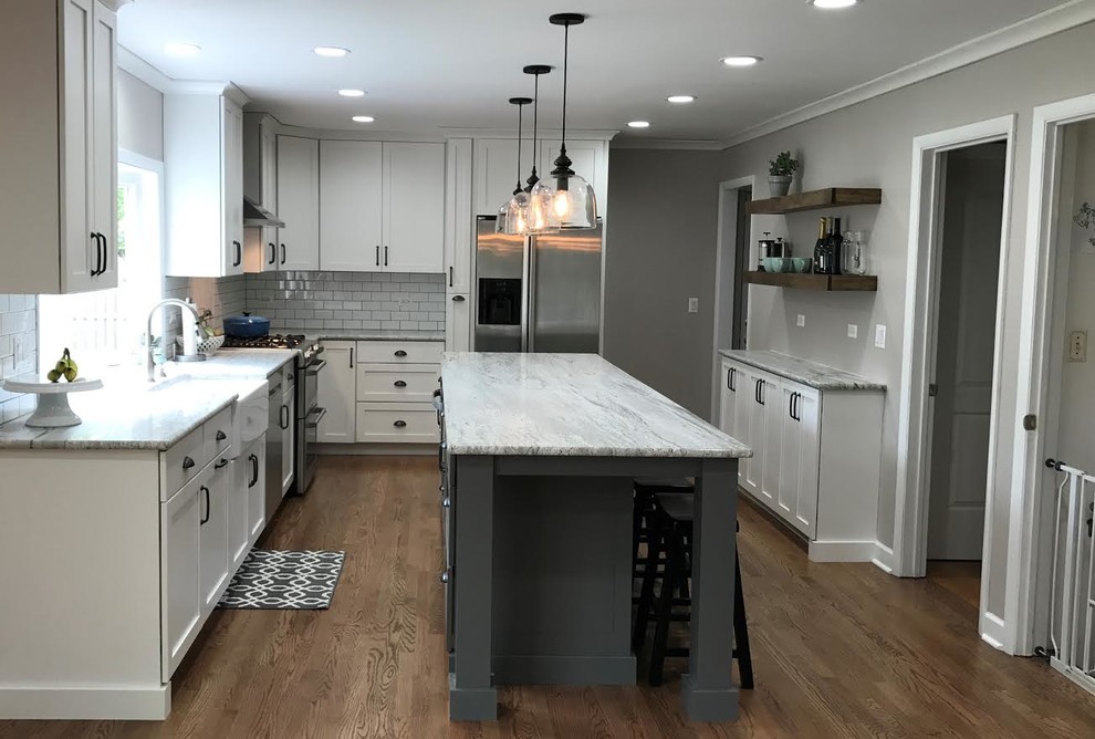 Design ideas for a mid-sized country l-shaped open plan kitchen in Chicago with a farmhouse sink, shaker cabinets, white cabinets, granite benchtops, white splashback, subway tile splashback, stainless steel appliances, dark hardwood floors, with island and brown floor.