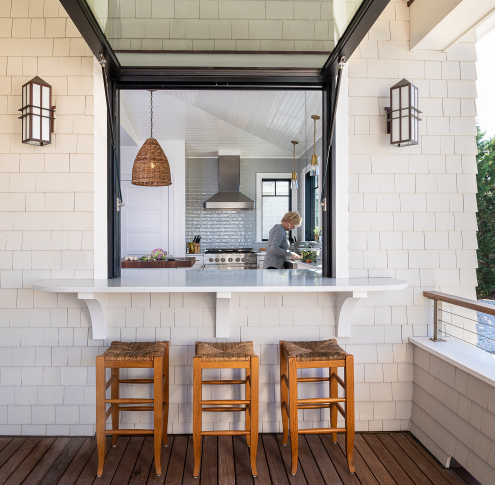 Cette image montre un grand porche d'entrée de maison avant marin avec une cuisine d'été, une terrasse en bois, une extension de toiture et un garde-corps en câble.