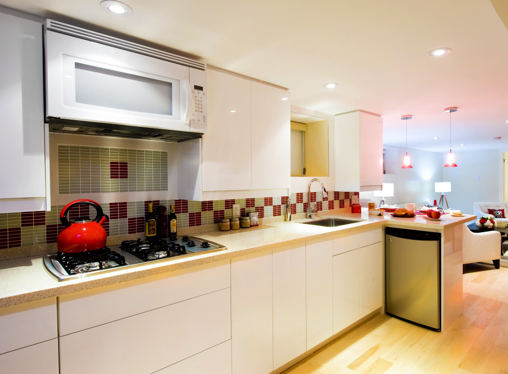 Medium sized modern l-shaped kitchen/diner in Toronto with flat-panel cabinets, white cabinets, multi-coloured splashback, stainless steel appliances, a breakfast bar, beige floors, multicoloured worktops, laminate floors, a submerged sink, engineered stone countertops and glass tiled splashback.