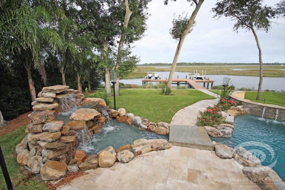 Design ideas for a large tropical backyard custom-shaped infinity pool in Jacksonville with natural stone pavers.