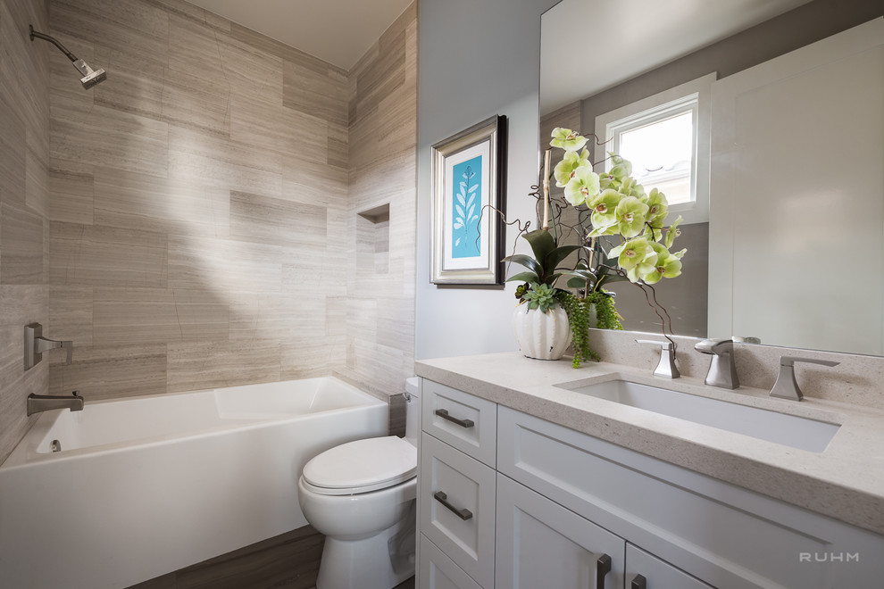 Photo of a small contemporary 3/4 bathroom in Orange County with an undermount sink, shaker cabinets, white cabinets, an alcove tub, a one-piece toilet, beige tile, porcelain tile, grey walls, a shower/bathtub combo, vinyl floors and solid surface benchtops.